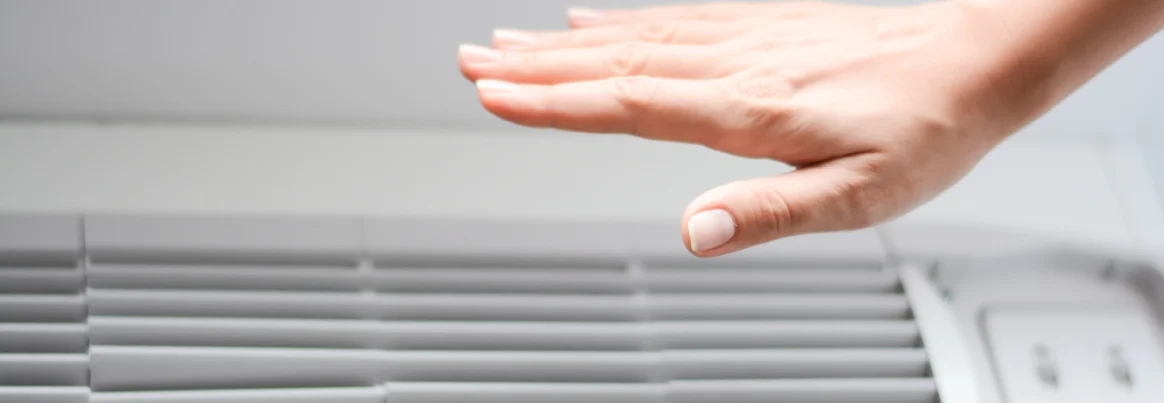 Eine Hand prüft die Kühlleistung einer Klimaanlage.